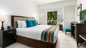 A hotel room with a bed, a desk, a chair, a TV, and a balcony with a view of palm trees. - Spa Suite Beach Club 3221 (Cairns)