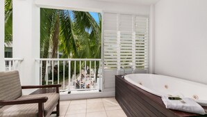A balcony with a view of palm trees, a wooden chair, and a large bathtub. - Spa Suite Beach Club 3221 (Cairns)