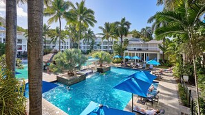 A resort pool area with multiple swimming pools, lounge chairs, and umbrellas. - Spa Suite Beach Club 3221 (Cairns)