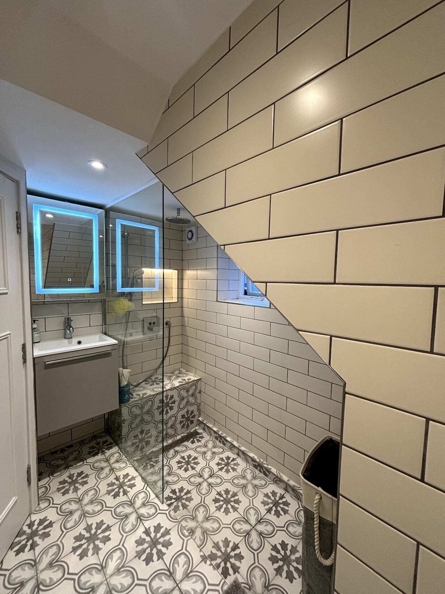 A bathroom with a white sink, a glass shower enclosure, and patterned floor tiles.