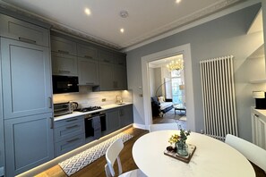 Una cocina moderna con armarios grises, una mesa de comedor blanca y una araña en la zona del comedor.