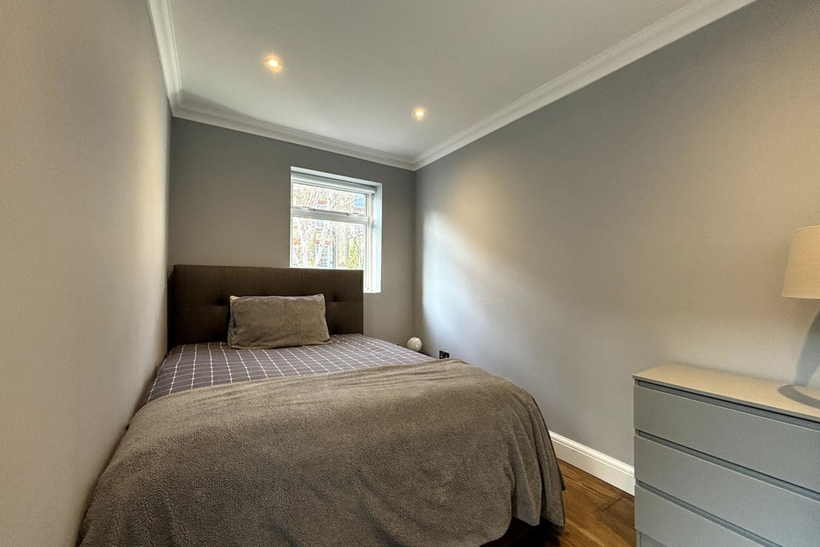 A bedroom with a bed, a nightstand, a dresser, and a window with a view of buildings.