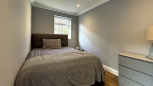 A bedroom with a bed, a nightstand, a dresser, and a window with a view of buildings. - Elegant & Beautifully Presented 1BD Flat- Chelsea! (London)