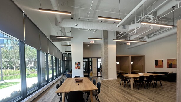 A spacious indoor area with large windows, wooden tables, and black chairs. - Chicago Shared Living Space with Office Space (Chicago)