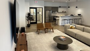 A modern living room with a sofa, coffee table, and chairs, a kitchen area with bar stools, and a flat-screen TV mounted on the wall. - Chicago Shared Living Space with Office Space (Chicago)