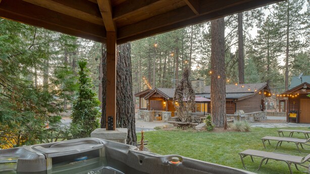 Ein Whirlpoolbereich mit einer Holzterrasse, umgeben von einem Wald, und ein kleines Gebäude mit Lichterketten.