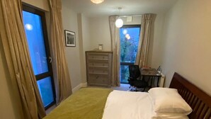 Un dormitorio con cama, cómoda, escritorio y ventana con cortinas.