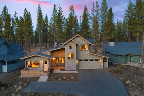 A modern two-story house with a garage, surrounded by tall pine trees.