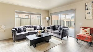 Un salon avec deux canapés gris, une table basse noire et un fauteuil rouge. Une porte-fenêtre coulissante donne accès à un balcon.
