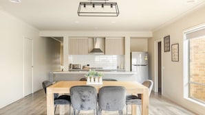 Une cuisine moderne avec des meubles de couleur bois clair, un îlot central et un coin repas comprenant une table en bois et des chaises grises.