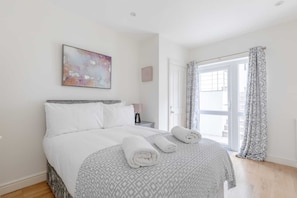 Un lit bien fait, recouvert d’une couvre-lit à motifs, une table de chevet avec une lampe et une grande fenêtre avec des rideaux.