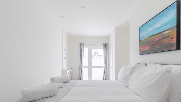 A hotel room with a large bed, a painting on the wall, and a view through the window. - Beautifully Presented 2BD Flat W/patio- Kensington (London)