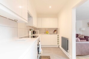 A modern kitchen with white cabinets, a countertop, and a radiator. - Beautifully Presented 2BD Flat W/patio- Kensington (London)
