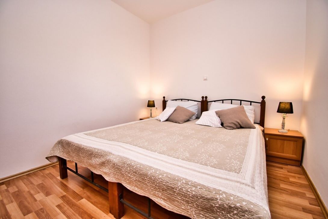 Una cama bien hecha con estructura de madera, una colcha estampada y dos lámparas de noche.