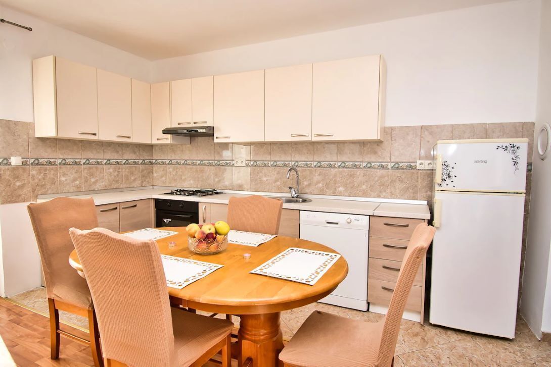 A modern kitchen with light-colored cabinets, a round wooden table, and beige chairs.