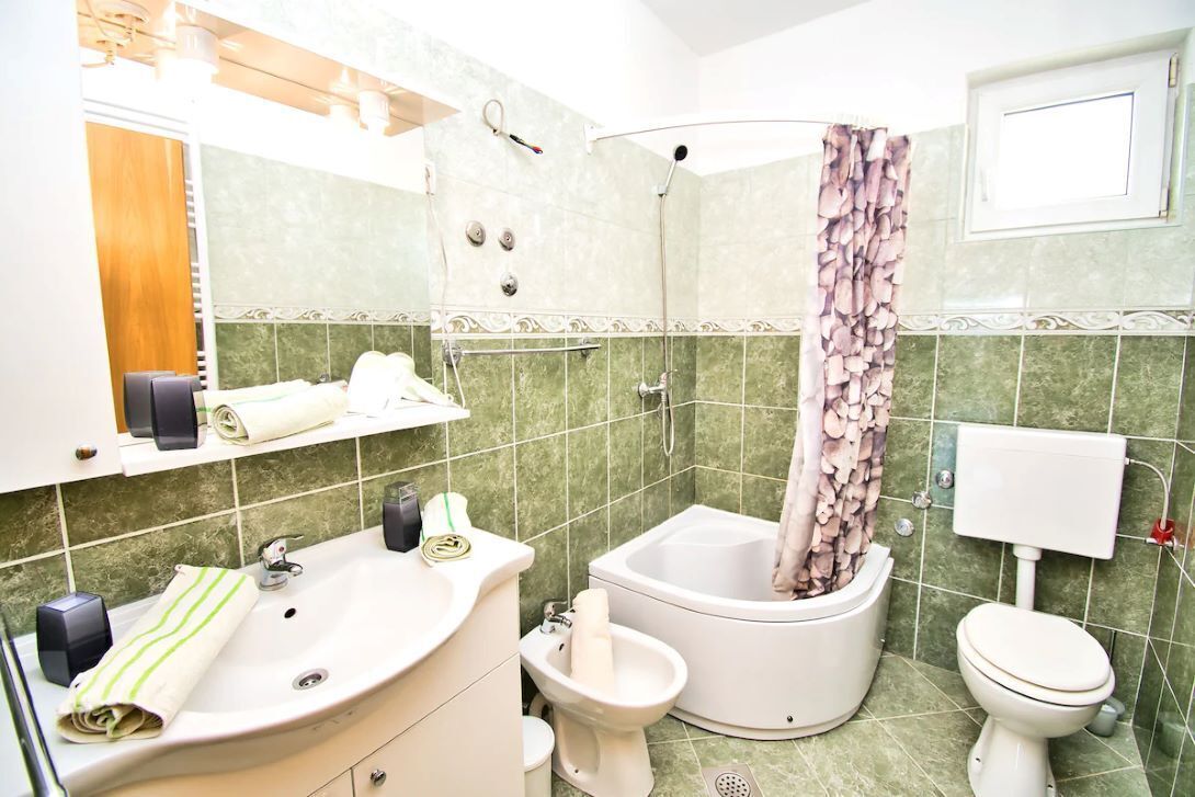Un baño con un lavamanos, dos inodoros, una ducha y un dispensador de papel higiénico.