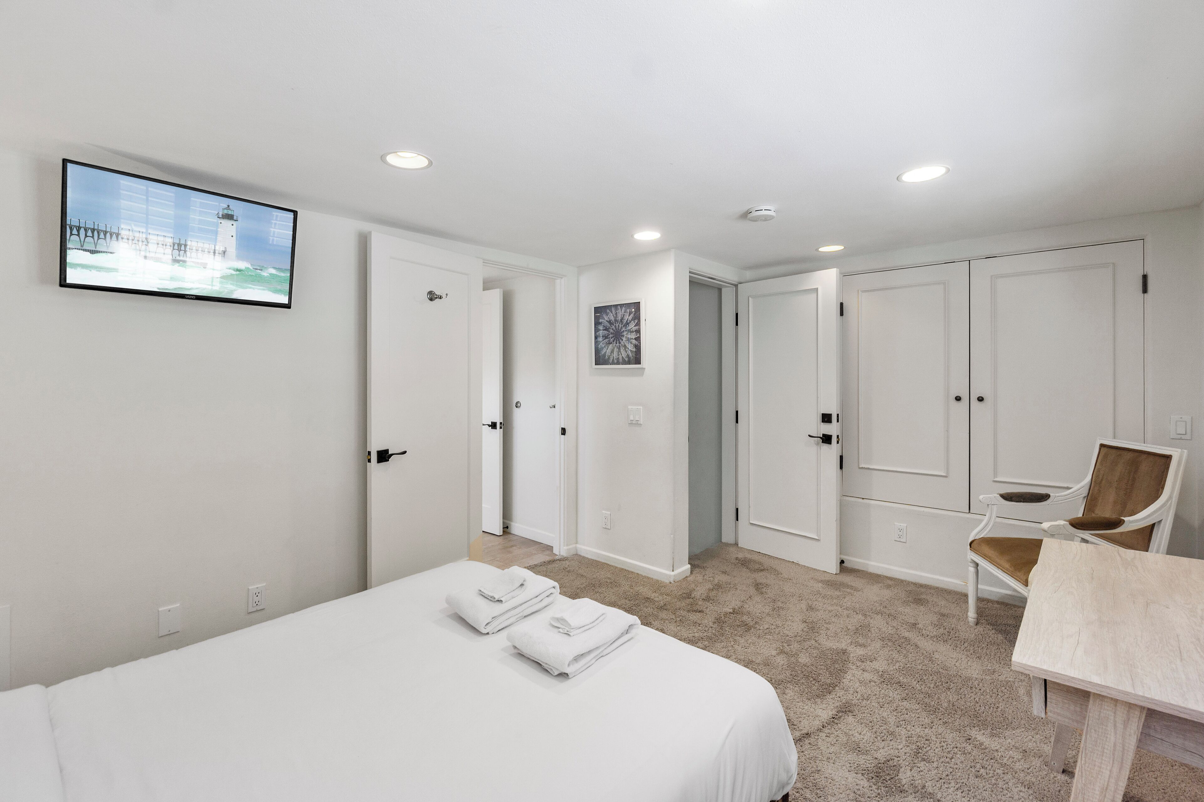 Una habitación de hotel con una cama, dos puertas blancas, un televisor en la pared, una silla y una mesita.