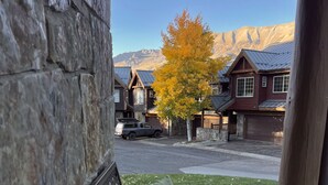 Un banc agrémenté d’un coussin sur lequel est écrit « Bienvenue », des murs en pierre, un arbre aux feuilles jaunes et, au fond, des maisons aux toits sombres.