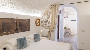A bedroom with a bed, a stone wall, a wooden door, and a dining area visible through an archway. - La Casa del 600 Sea View on the Amalfi Coast, with patio and garden (Tovere (San Pietro))