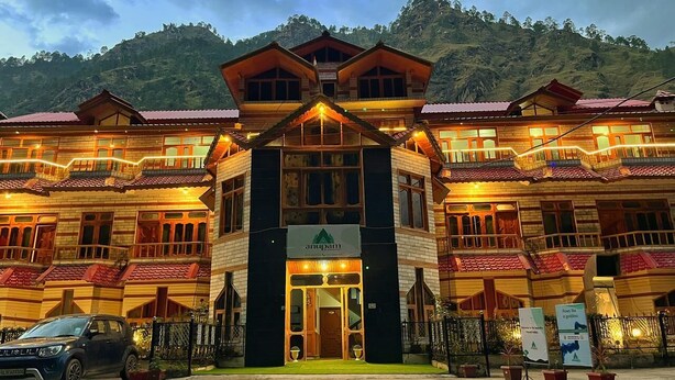 A multi-story hotel with a central entrance, surrounded by a fence, and set against a mountainous backdrop. - Hotel Anupam  (Bhuntar)