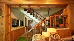 A wooden interior with a staircase, wicker chairs, and a green carpet. - Hotel Anupam  (Bhuntar)