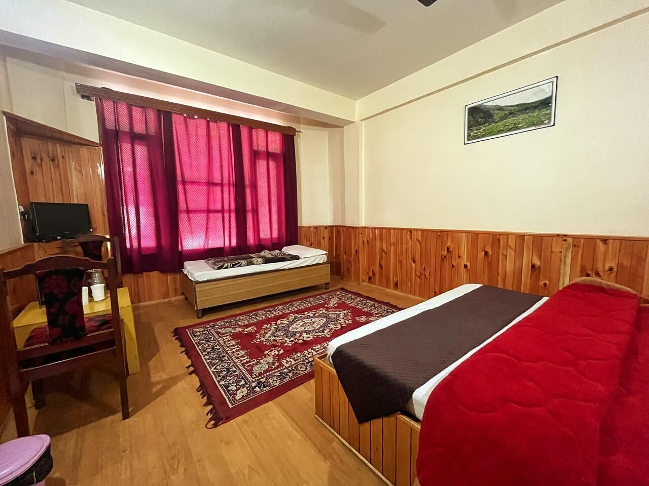 Una stanza arredata con un letto, un armadio in legno, una scrivania con sedia, una finestra con tende e un quadro appeso al muro.