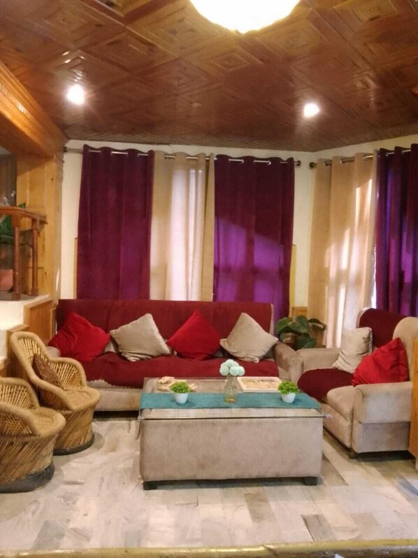 A cozy living room with a red sofa, two armchairs, a wooden coffee table, and a ceiling with a wooden panel design.