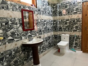 Un baño con lavamanos, inodoro y ducha. Las paredes presentan un diseño geométrico de azulejos.