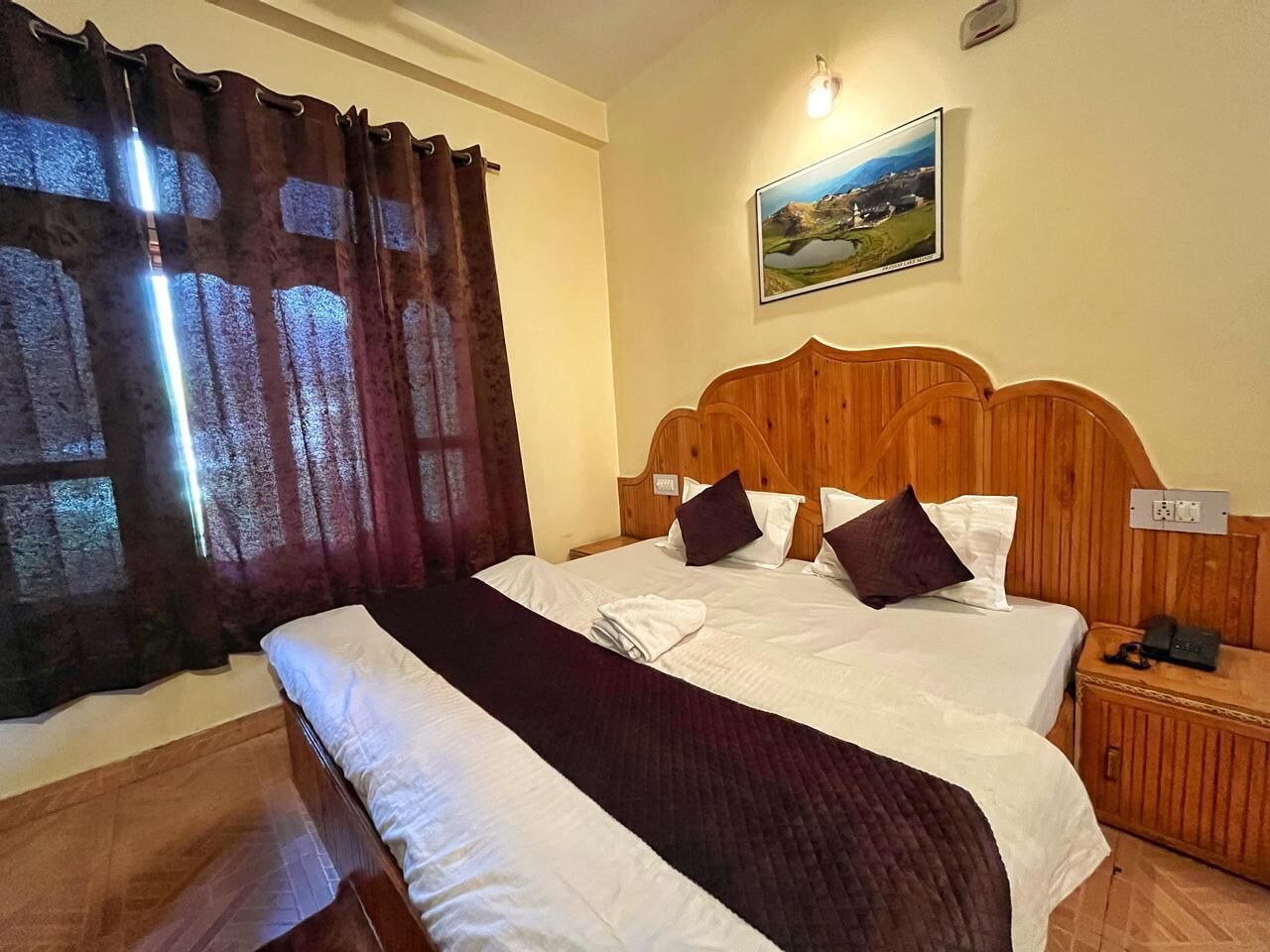 Habitación de hotel con una cama grande, cabecera de madera y vistas a un paisaje a través del ventanal.