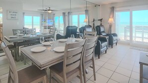Un coin repas avec une table dressée pour quatre personnes, un téléviseur en arrière-plan et un balcon avec vue.