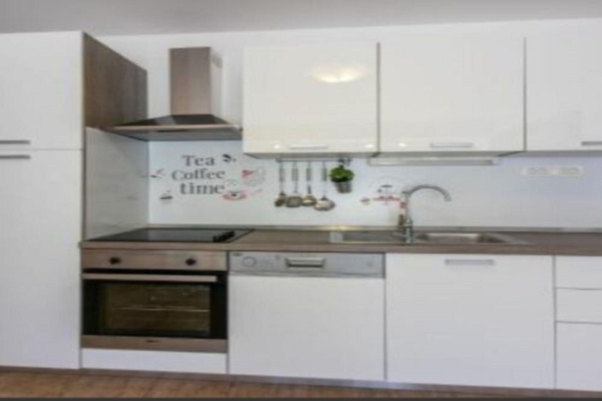 Een moderne keuken met witte kasten, een roestvrijstalen oven, een vaatwasser, en een bordje met de tekst 'Tea & Coffee time'.