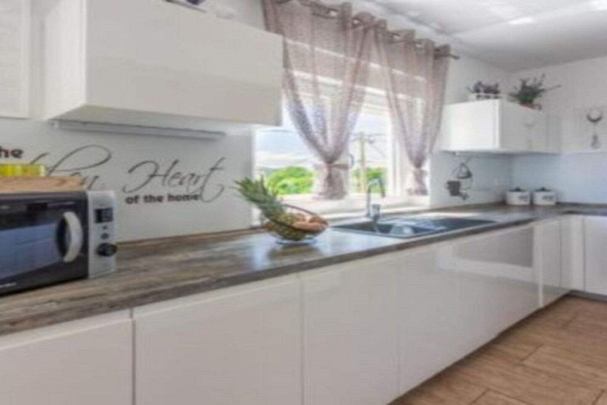 Cozinha moderna com armários brancos, um micro-ondas e uma tigela de frutas no balcão.