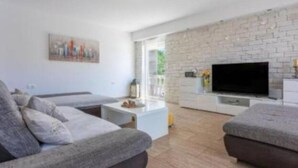 Una sala de estar moderna con un sofá gris, un televisor de pantalla plana montado en una pared de ladrillo blanco y una pequeña mesa de centro.