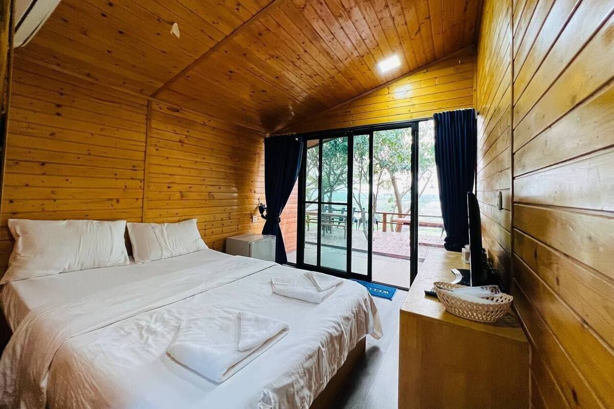 Une pièce de style cabane en bois, avec un grand lit, une petite table et une fenêtre avec des rideaux.