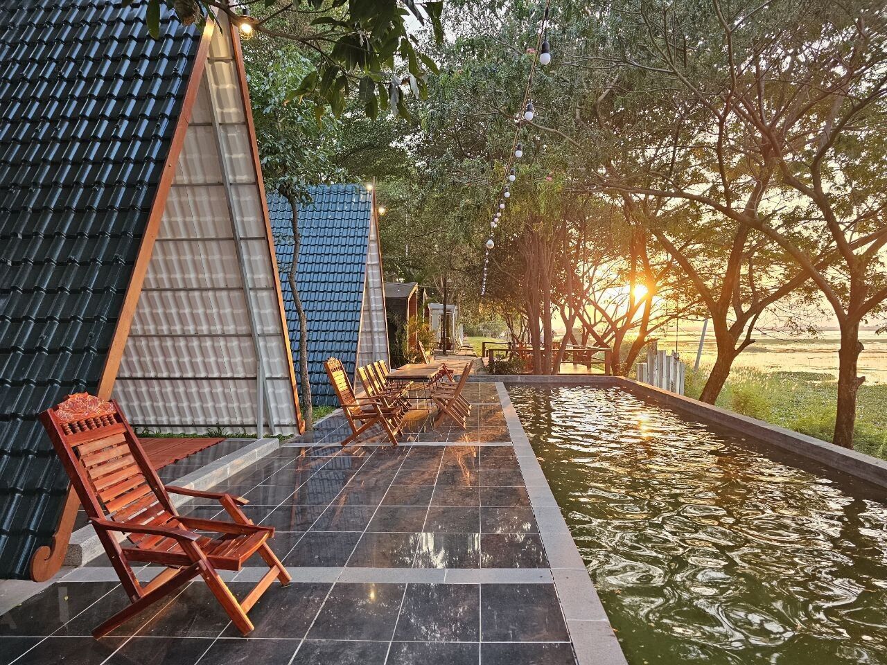 A poolside area with a tiled deck, wooden lounge chairs, and a small table.