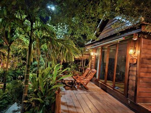 A wooden deck with lounge chairs and a glass-enclosed room, surrounded by lush tropical plants. - Chomka Thnong Resort (Khsach Kandal)