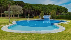 Una piscina de forma circular, rodeada por un césped cuidado y árboles.