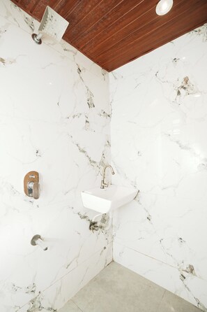 Un bany amb un lavabo de marbre blanc, sostre de fusta i plat de dutxa amb aixeta manual.