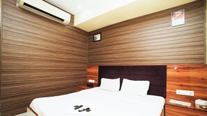 A hotel room with a wooden panel wall, a bed with white bedding, a wooden headboard, and a nightstand with a phone and a tissue box. - Hotel Twigo Inn (Mumbai)