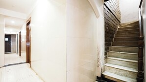 A hallway with a marble floor leading to a staircase with wooden steps and a dark wooden handrail. - Hotel Twigo Inn (Mumbai)