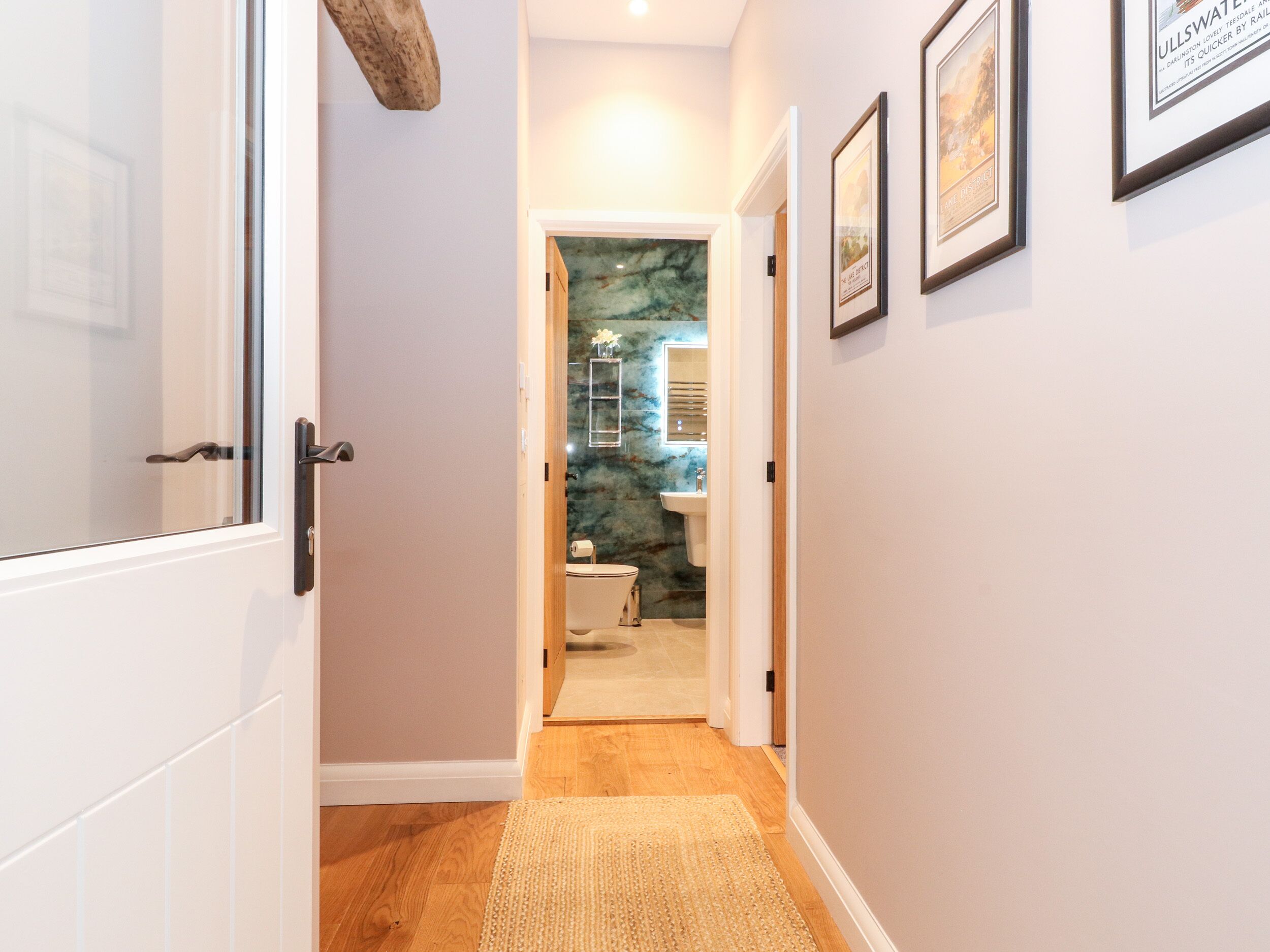 A hallway with a wooden floor, a rug, and a bathroom visible through an open door.