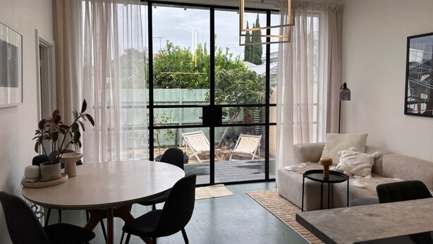 Un salon moderne doté d’une grande porte-fenêtre coulissante donnant sur un balcon, d’une table à manger ronde et d’un canapé.