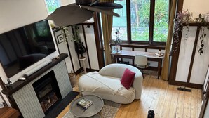 Un salon chaleureux avec une cheminée, des sièges confortables et une grande fenêtre donnant sur un paysage verdoyant.