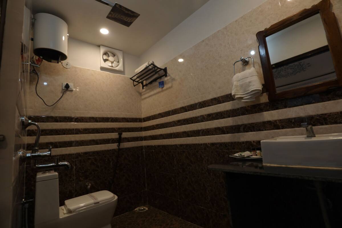 Ein Badezimmer mit Toilette, Waschbecken und Spiegel. Ein Handtuchhalter mit einem daran hängenden Handtuch ist vorhanden. Die Wände haben ein Streifenmuster.