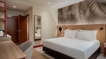 Habitación de hotel con una cama grande, un escritorio de madera, una silla, un espejo y un muro con diseño de hojas.