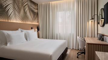 A modern hotel room with a large bed, a desk, and a chair.