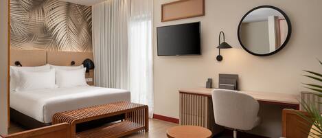 Una habitación de hotel moderna con una cama grande, un escritorio, una silla, un espejo redondo y un televisor.