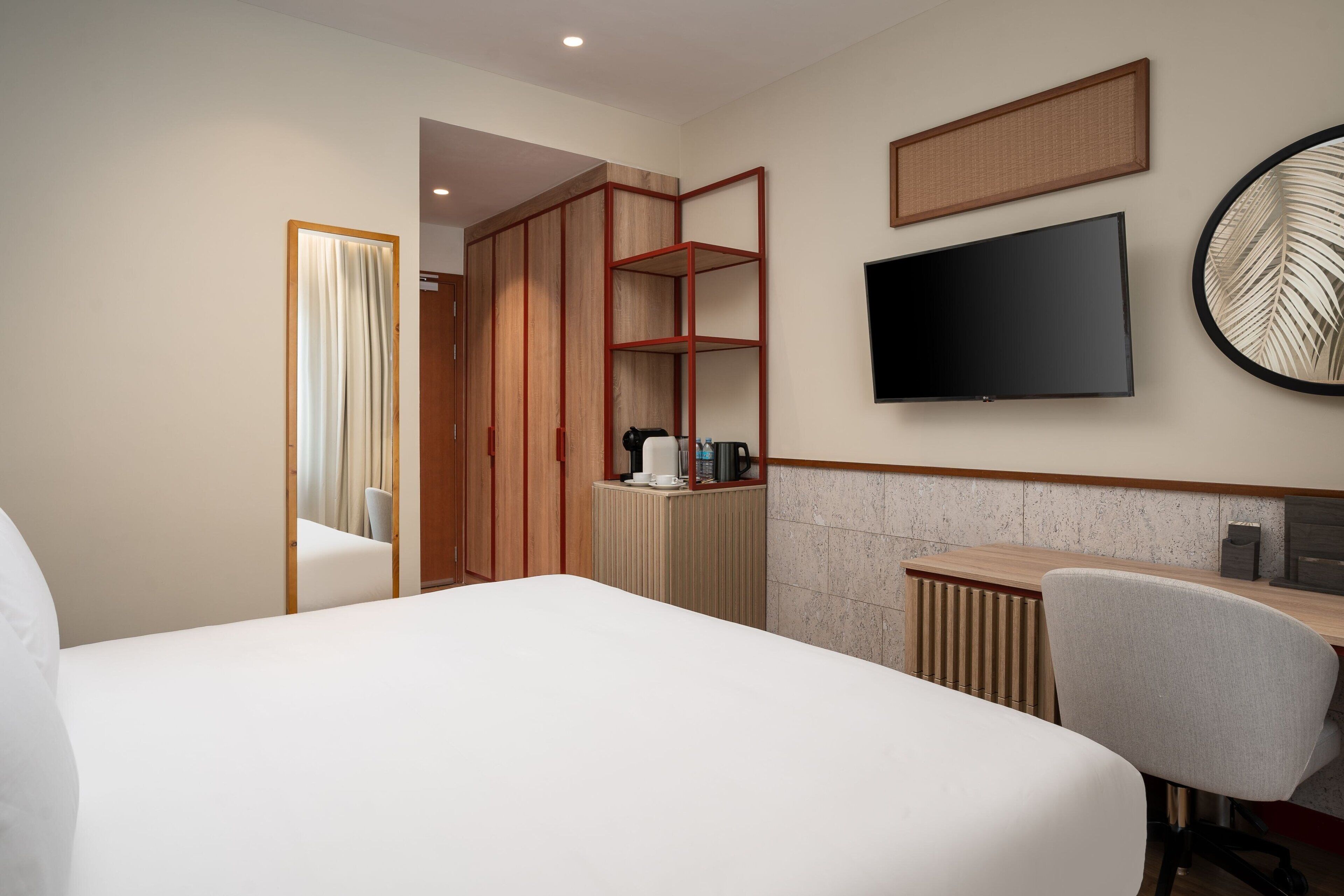 A hotel room with a bed, a desk, a TV, and a wardrobe.