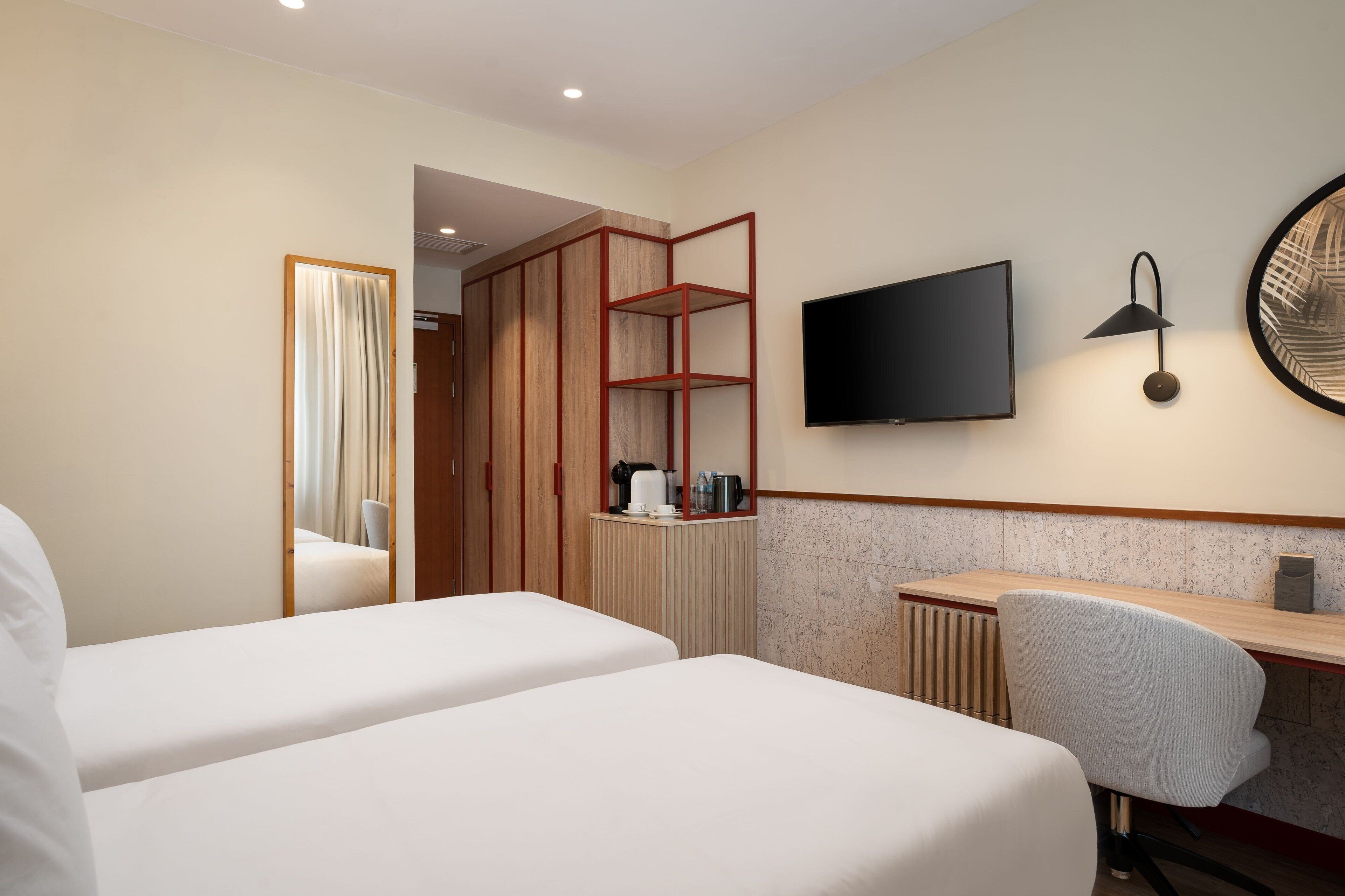 Habitación de hotel con dos camas, un escritorio, una silla, un televisor y un espejo.