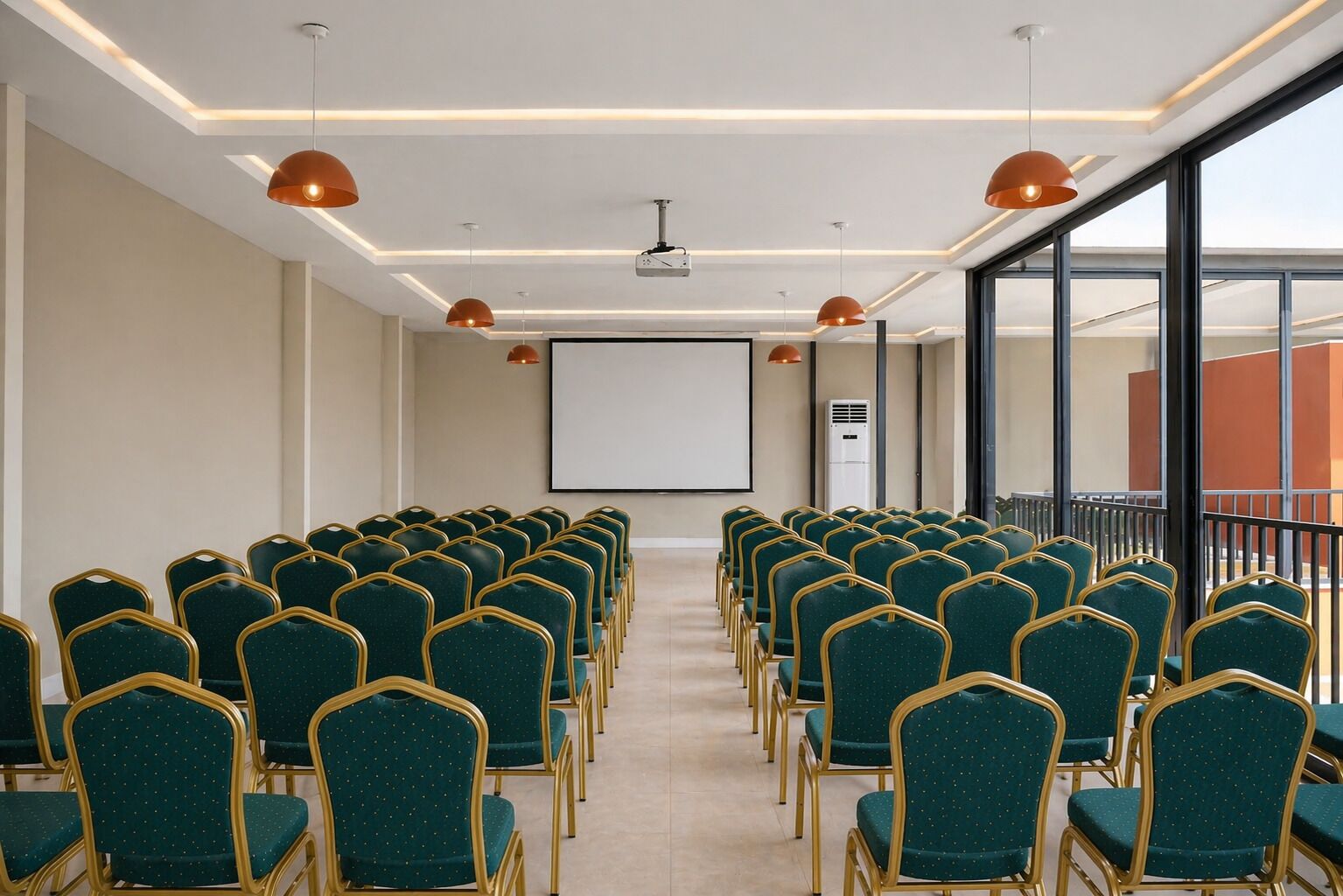 Un salón de conferencias con filas de sillas verdes, una pantalla de proyector e iluminación colgante.
